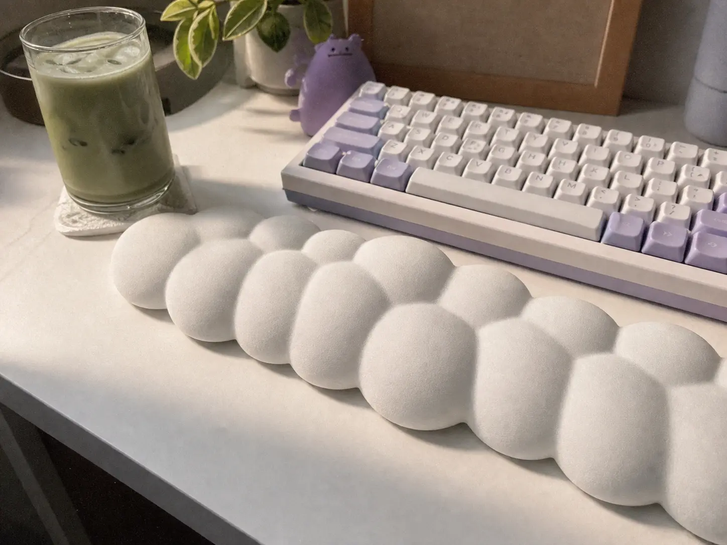 White cloud shaped wrist rest placed in front of a keyboard with an iced matcha latte