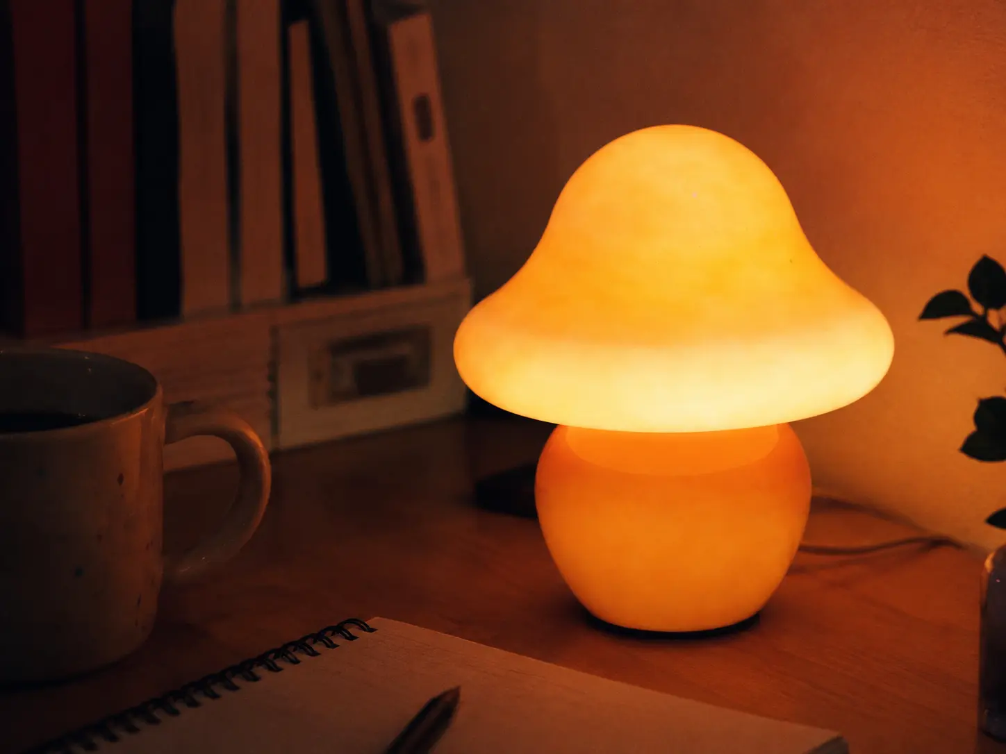 Photorealistic close-up of a cozy glowing mushroom desk lamp on a wooden desk with warm ambient lighting