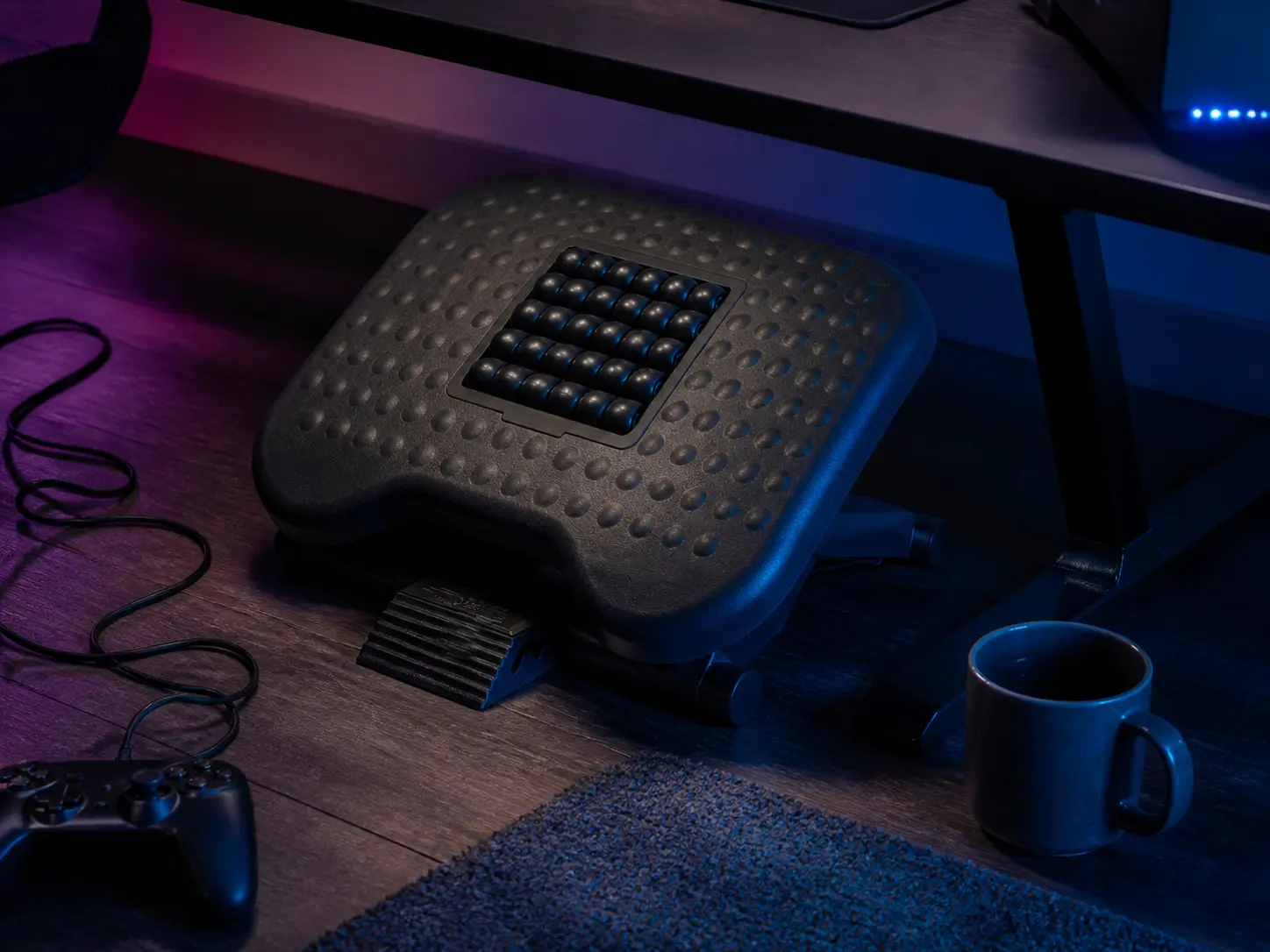 Adjustable black ergonomic footrest with massage rollers under a gaming desk