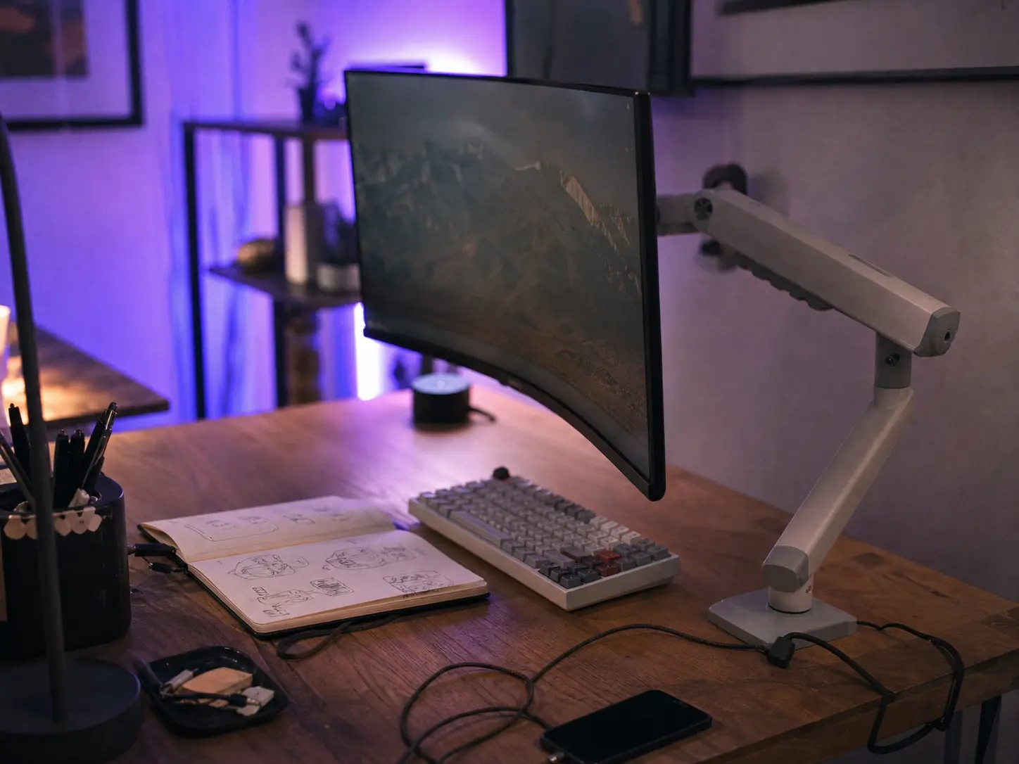 Sleek white single monitor mount suspending a curved screen over a cozy wooden desk setup with soft purple lighting