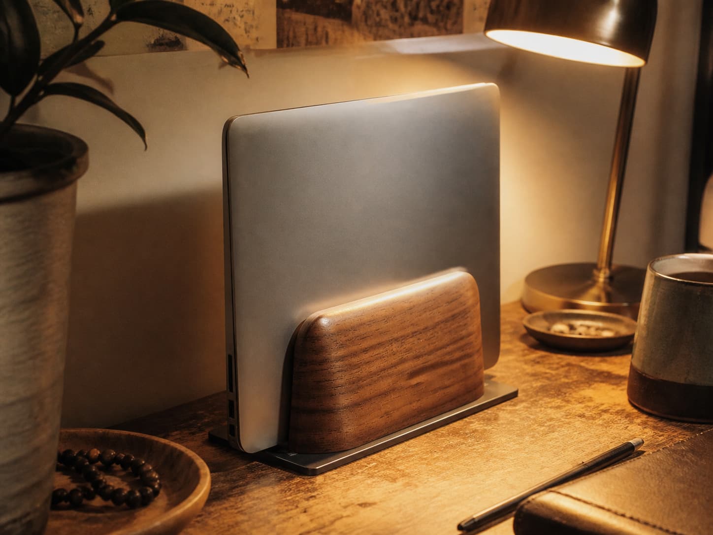 Walnut wood vertical laptop stand holding a closed laptop on a cozy desk