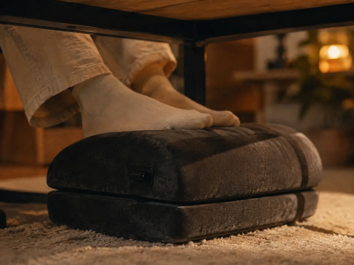 First person view under a cozy desk looking at a plush velvet memory foam footrest on a soft rug