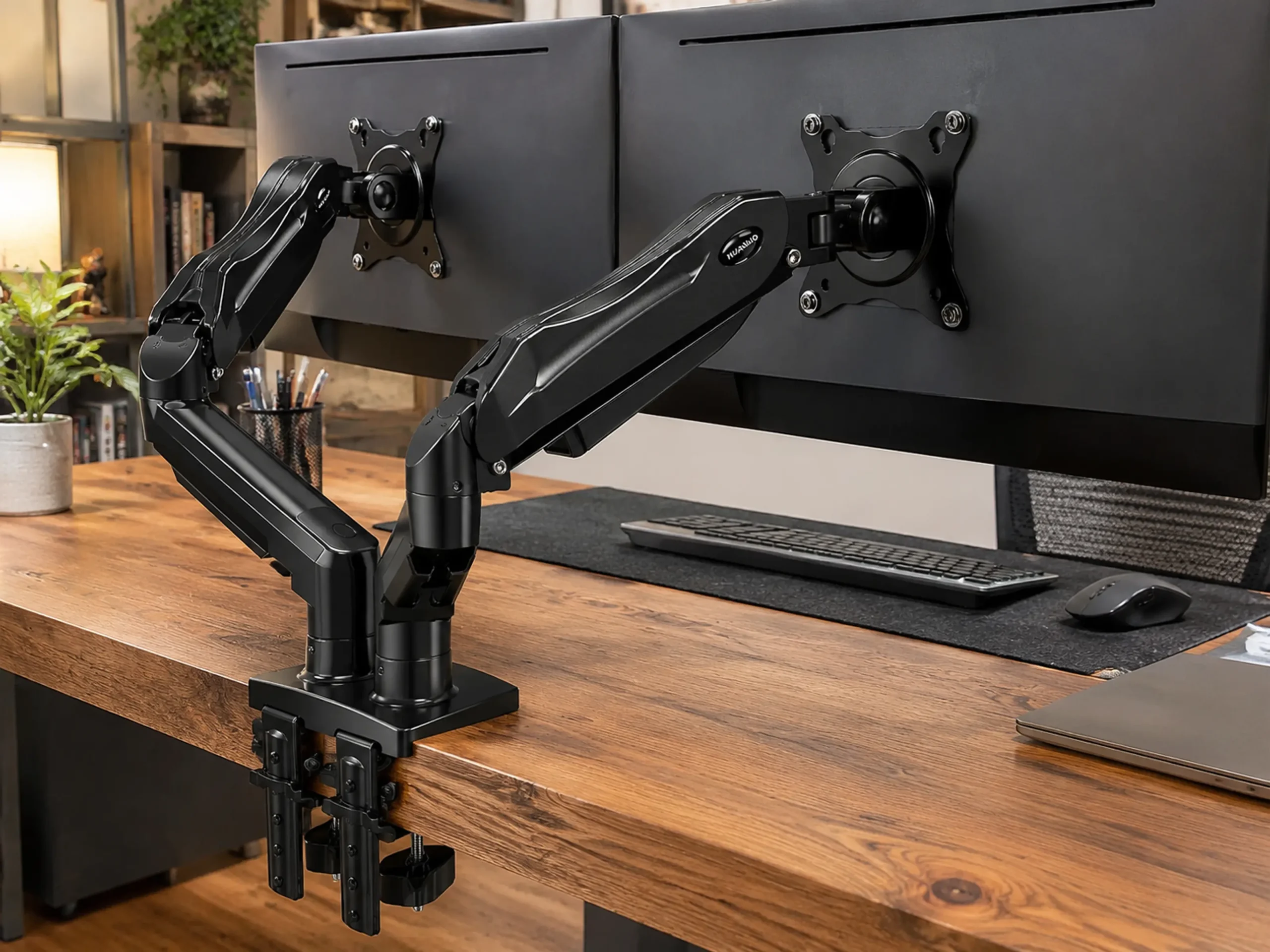 Close-up of a heavy-duty dual monitor arm C-clamp on a thick wooden desk